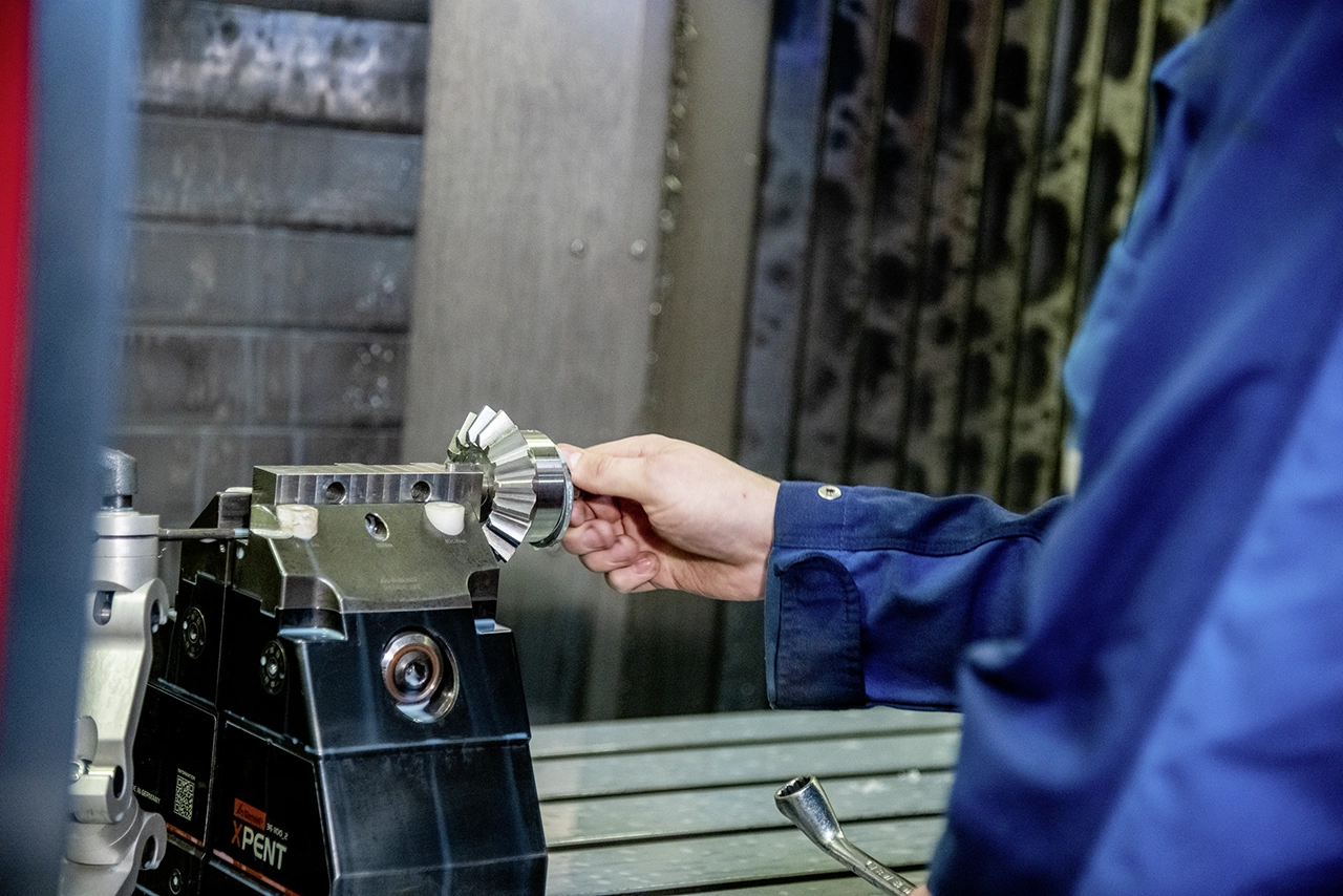 Ein Mitarbeiter platziert ein Zahnrad präzise in eine Spannvorrichtung auf einer CNC-Fräsmaschine. Die Szene zeigt höchste Sorgfalt bei der Vorbereitung eines Werkstücks zur Bearbeitung.