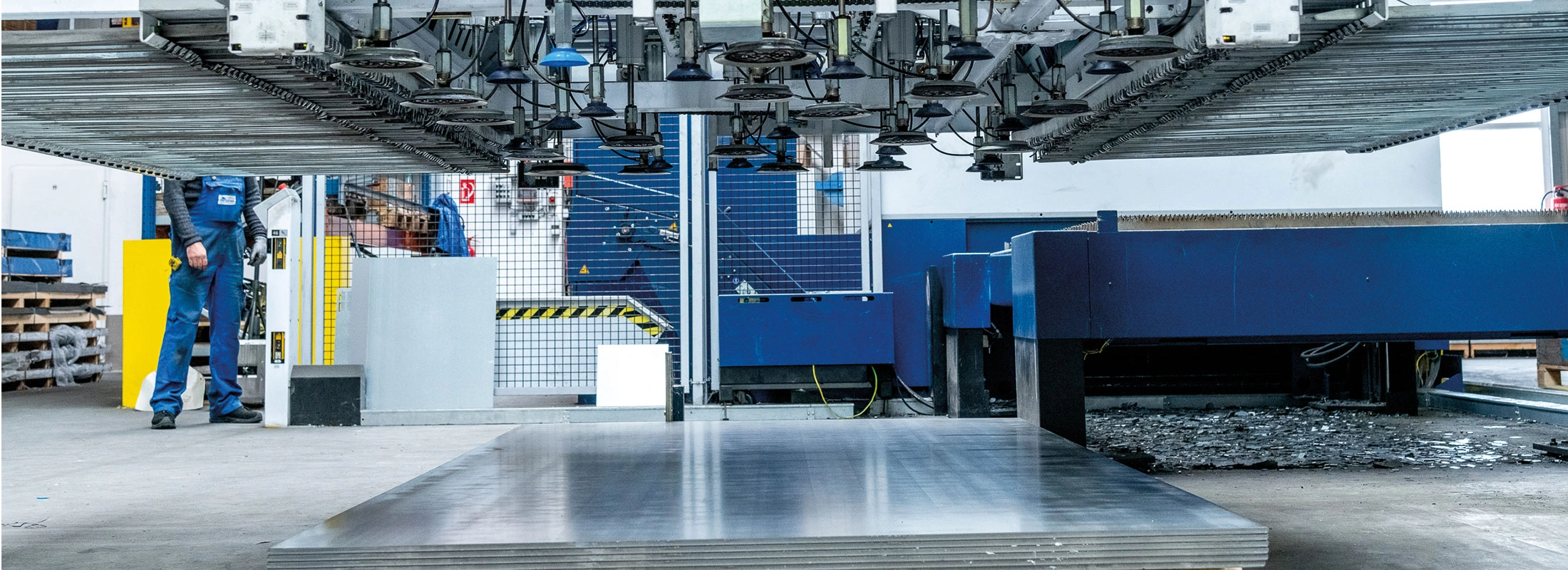 Moderner Maschinenpark mit automatisierter Blechverarbeitung und Vakuumhebern – ein Mitarbeiter überwacht den Fertigungsprozess.